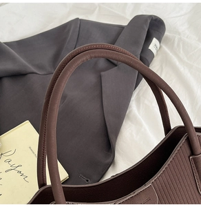 Détail d'un sac seau en cuir marron avec surpiqûres verticales sur un blazer gris