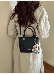 Detail of a black faux leather bucket bag with a cute teddy bear charm on beige coat