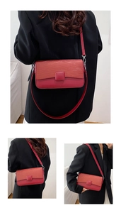 Detail of red textured leather flap bag with square buckle on a black suit background