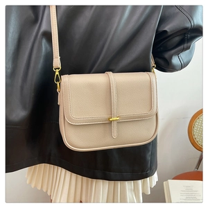 Détail du sac bandoulière crème en cuir grainé porté par un mannequin avec boucles dorées