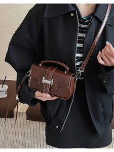 Macro detail of dark brown polished leather bag featuring a silver metal buckle closure