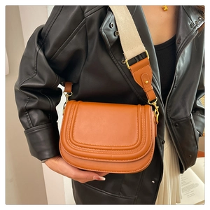 Détail du sac selle marron avec large bandoulière tissée et finitions métalliques
