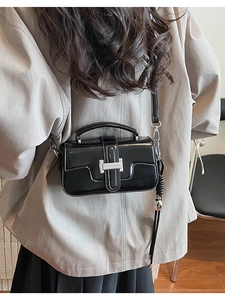 Detail of black glossy crossbody bag with silver lock and woven ball charm on a model