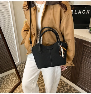 Détail d'un sac cabas noir avec pendentif perlé porté en bandoulière sur un mannequin