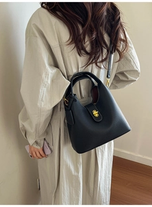 Close-up of black litchi grain leather bucket bag with gold lock on a model