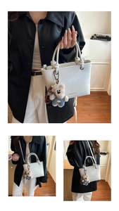 Detail view of a white leather bucket bag featuring a teddy bear charm and logo print