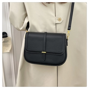 Détail du sac bandoulière noir texture litchi et boucle dorée sur manteau blanc