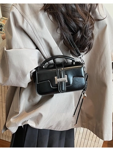 Black square crossbody bag on a model wearing a beige trench coat showing style