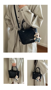 Detail of black leather bucket bag featuring round handles and a cute teddy bear charm