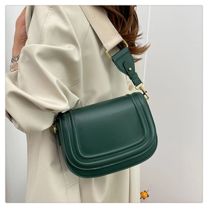 Détail du sac selle vert foncé avec bandoulière beige et finitions dorées chic