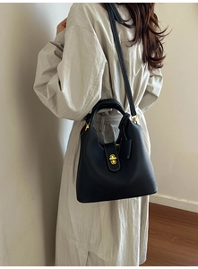 Detail of black lychee grain leather bucket bag with gold lock worn with a beige coat