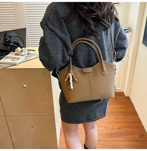 Detail der khakifarbenen Ledertasche mit Holzperlenanhänger und Metalllogo im Büro