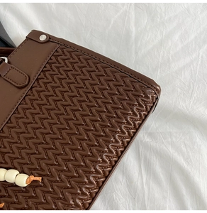 Close-up of wavy quilted dark brown leather handbag with metal studs and bead tassel detail