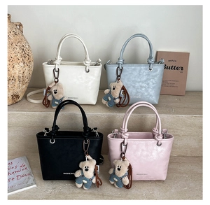 Close-up of four colors of faux leather bucket bags with plush bear charms and branding