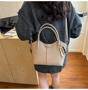 Detail der beigen Vintage-Eimertasche aus weichem Leder mit vertikaler Prägung und Perlenanhänger