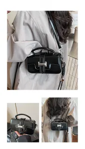 Detail of a black glossy crossbody bag featuring a silver square buckle and top handle