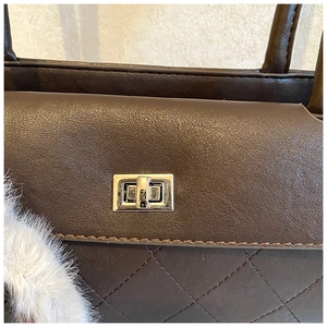 Detail of dark brown quilted handbag with gold clasp and white faux fur keychain