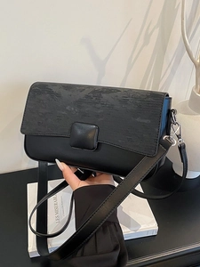 Minimalist black flap crossbody bag featuring embossed texture and square decorative buckle