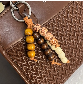 Detail of dark brown quilted leather handbag with colorful bohemian wooden bead charm