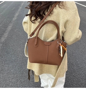Détail du sac seau en cuir marron avec charme en perles de bois et rayures verticales