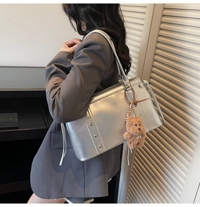 Detail of silver metallic tote bag with decorative rivets and brown plush bear charm