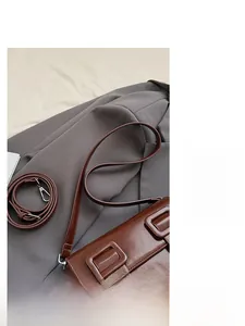 Detailed view of deep brown saddle bag on grey blazer showing texture and twin square buckles