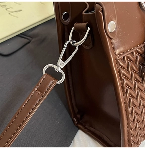 Detail of woven brown leather handbag featuring silver lobster clasp and precise stitching