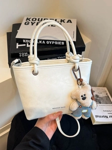 White PU leather bucket bag with rope knot handle and plush bear charm on books