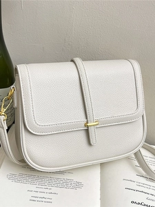 Sacoche blanche en cuir litchi avec boucle dorée posée sur un livre ouvert