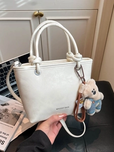 Cream white bucket bag with knot handle and teddy bear charm on premium leather background