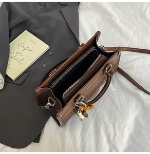 Detailed top view of dark brown leather handbag with woven texture and bead charm