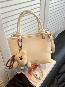 Minimalist beige bucket bag with knot handle and cute bear charm shown in lifestyle setting