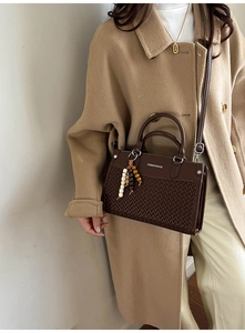 Detail of dark brown handbag with V-weave texture and bead tassel held by a model