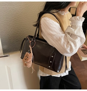 Detail of glossy leather tote bag with stud accents and a plush bear charm on a model
