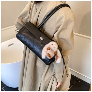 Detail of black quilted shoulder bag with flip-top lock and cute plush rabbit charm