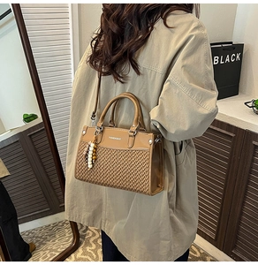 Close-up of brown woven leather bag with unique pendant held by a model in soft indoor light
