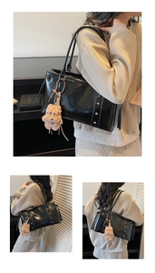 Detail of black leather tote bag with silver studs and a plush bear charm on a model