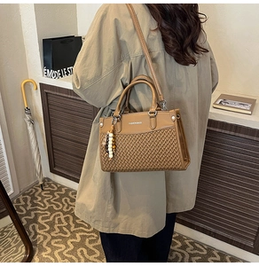 Detail of a brown PU handbag featuring V-pattern weaving and beaded decorative pendant