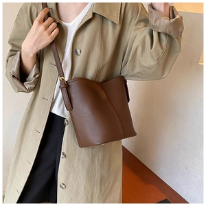 Detail of dark brown lychee textured bucket bag with adjustable strap on trench coat