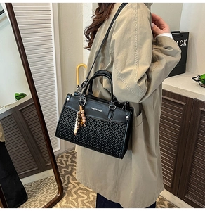 Detail of black woven patchwork handbag with round handles and wooden bead charm