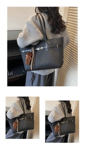 Detail of black leather tote bag with metal buckle, plush bear charm, and long tassels