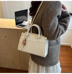 Detail of cream crossbody bag featuring woven texture, silver lettering, and beaded charm