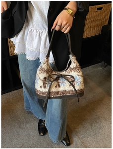 Detail of plush geometric patterned tote bag with dark bow and leather handle worn on shoulder