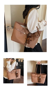 Detail of large brown tote bag with decorative strap and plush bear charm worn by model