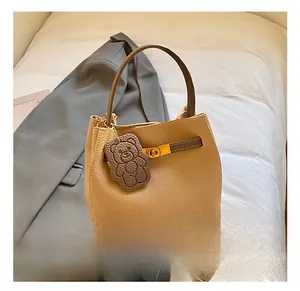 Détail du sac seau en cuir beige avec poignée marron et accessoire ours charmant