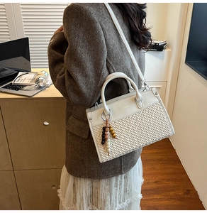 Detail view of white woven PU leather handbag with beaded pendant in a modern office setting