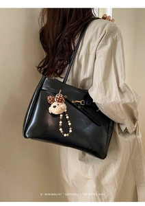 Detail of black leather tote bag with decorative buckle and beige plush bear charm
