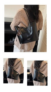 Detail of glossy black tote bag with shoulder straps and brown charm on female model