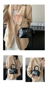 Detail of a black semi-circular crossbody bag with decorative buckle and slim strap