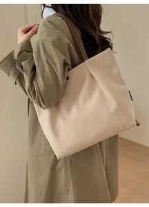 Detail view of large beige canvas tote bag with brown leather strap on a model shoulder